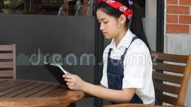 泰国学生十几岁的漂亮女孩用她的平板电脑坐在公园里。